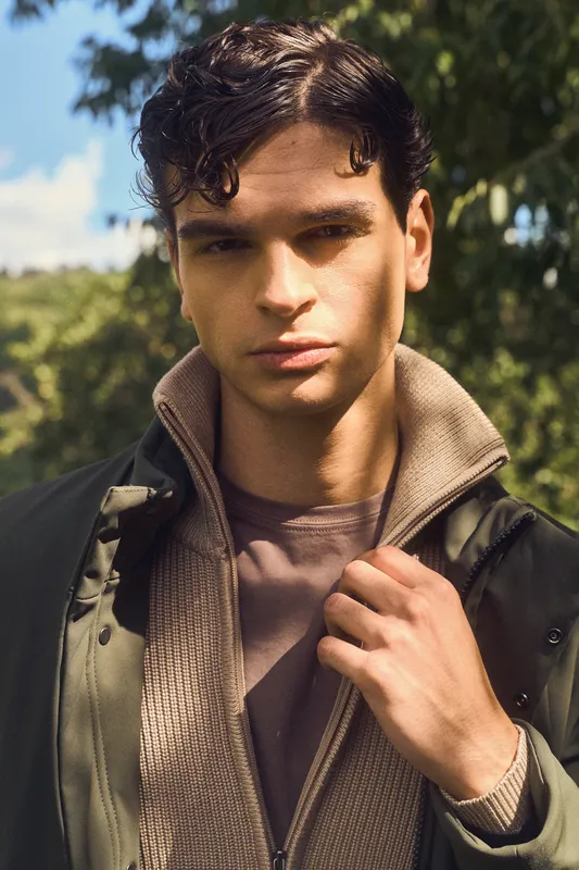 Primo piano di un ragazzo con giacca verde oliva e cardigan con zip