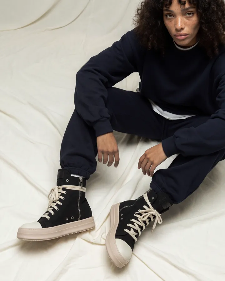 Ragazza con tuta blu notte seduta su un telo color crema, con sneakers alte