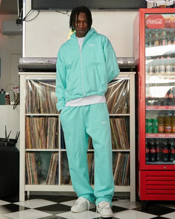 Ragazzo in tuta verde acqua accanto a una parete di dischi e a un frigo di bibite