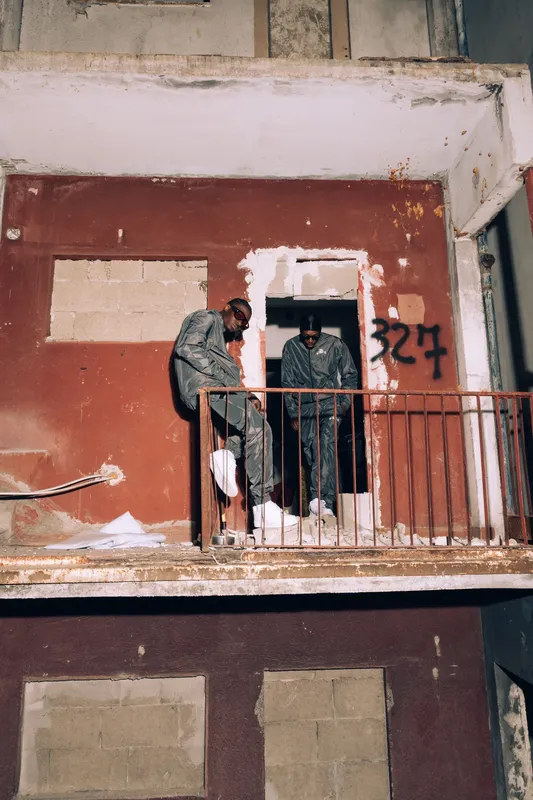 Due ragazzi in tuta su un balcone rosso scrostato